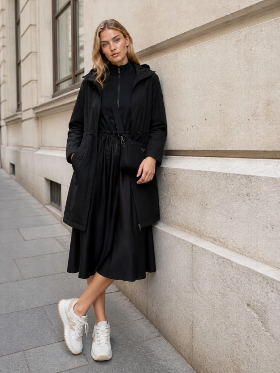 This look builds a sleek, urban uniform around the black Moncler parka, pairing it with a coordinating black technical midi dress for a long, streamlined silhouette that feels both utilitarian and quietly luxurious. Off-white and beige runners soften the darkness and underline the sporty SS attitude, while the precise Prada cross-body injects a subtle high-fashion note without breaking the minimalist, city-commuter aesthetic. Choosing the dress path keeps the outfit crisp and unfussy, avoiding the visual bulk that a separate top and bottom would add under the mid-length coat.