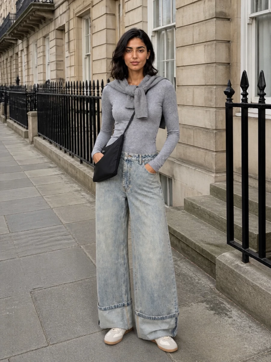 A heather grey bodysuit tucks into ultra-wide, faded denim for a low-slung, slouchy proportion that still feels clean and deliberate. Cream and grey sneakers keep the palette quiet and modern, while a slim black cross-body and soft grey neck wrap add just enough structure and texture for city days. The result is a minimalist streetwear uniform that feels easy to live in yet considered from every angle.