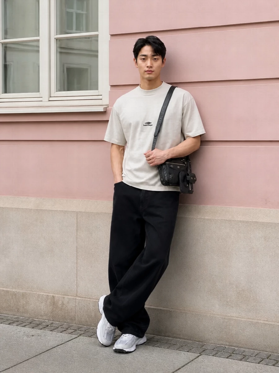 Balenciaga’s off white tee sits over long, puddled black denim for a clean, quietly graphic street uniform. White technical runners lighten the base and keep everything agile. A compact black crossbody finishes the monochrome palette with just enough texture and hardware to feel intentional without breaking the minimal mood.