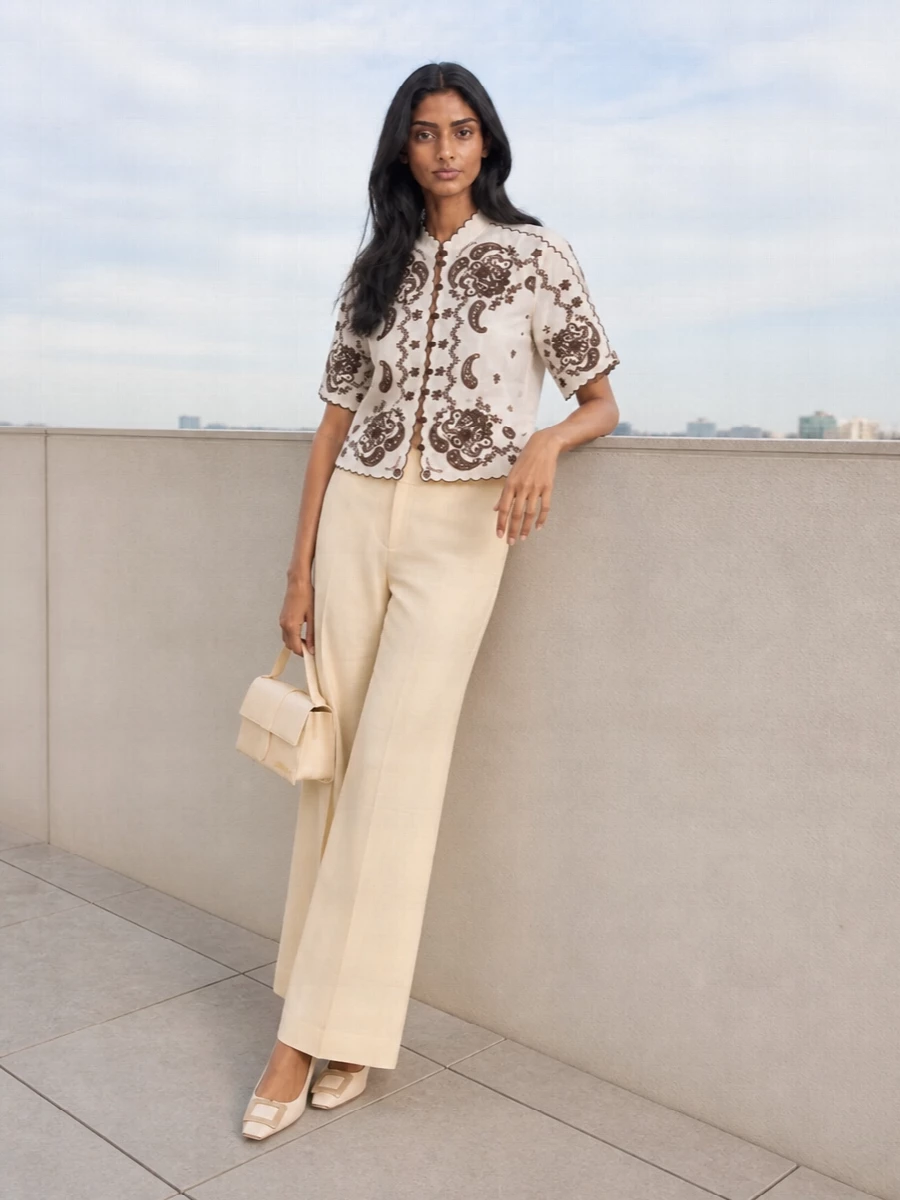 A romantic Zimmermann blouse is grounded with fluid buttercream tailoring for a soft, elongated silhouette in shades of ivory and chocolate. A sculpted ivory pump and structured mini top-handle keep the mood refined yet relaxed, perfect for long lunches or garden-party dinners.