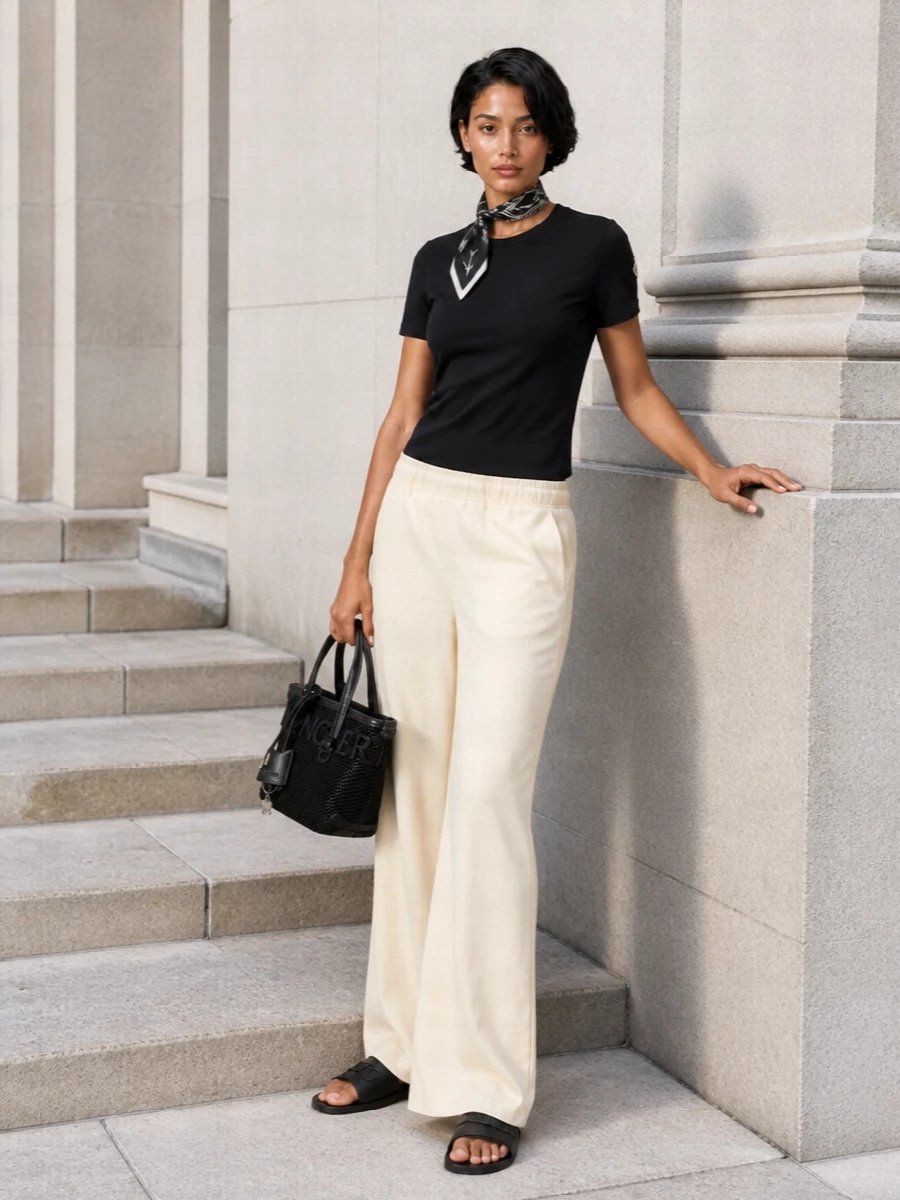 A black Moncler tee meets buttercream wide-leg trousers for a clean, sport-informed take on city dressing. Black slides and a structured mini tote sharpen the contrast, while a small monochrome silk scarf adds just enough graphic detail without disturbing the calm palette.