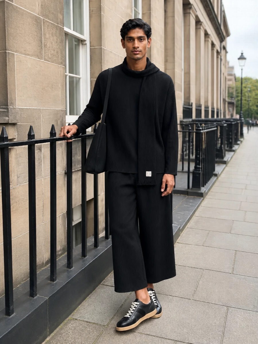 A full Homme Plissé set in deep black turns everyday dressing into a single, sculpted gesture. The wide, cropped pleated trouser and matching long-sleeve top read clean and architectural, yet move lightly with the body. Charcoal-grounded Margiela sneakers and a pleated bucket bag keep the story low-key and functional, all in a monochrome palette that feels calm rather than severe.