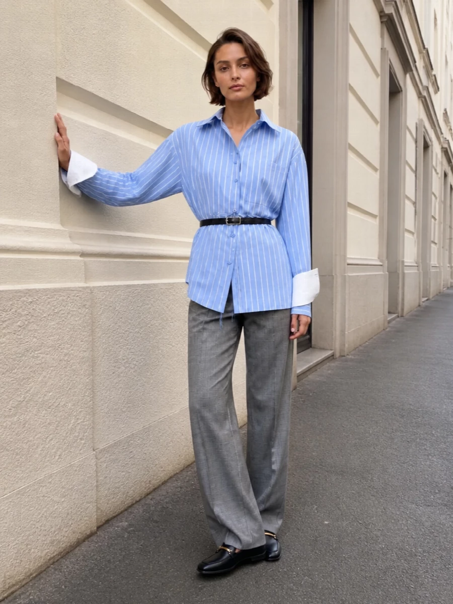Sportmax’s grey plaid trouser meets a cinched, sky blue stripe shirt for a fresh take on tailored, preppy polish that still feels properly office ready. Grounding it with sleek Tod’s loafers and a structured black Zanellato top-handle keeps the mood quietly decisive from client meetings through to late dinners. A slim black belt is the only punctuation, sharpening the high waist and letting the clean lines do the talking.
