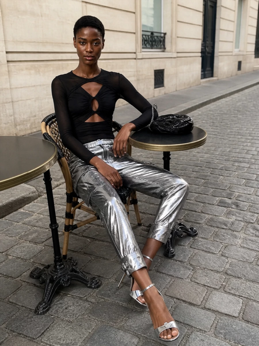 High-rise metallic cargos meet a sheer, cut-out black top for a sharp, nightlife-focused mix of space-age shine and body-conscious attitude. Silver stilettos extend the chrome story, while a black chain-strap baguette and slim linked belt add just enough hardware to keep it street without losing polish. The result is a tight, leg-lengthening silhouette that feels unapologetically after dark and very Paris club-kid.