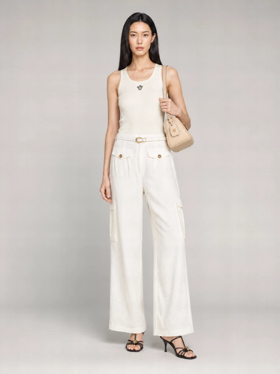 Soft off white tailoring meets quiet Versace glamour in a clean, column silhouette. The buttercream ribbed tank keeps the upper half close to the body, so the wide-leg trouser can move with fluid ease. Black strappy sandals and a beige shoulder bag introduce subtle contrast and gold accents, keeping the outfit city-ready from daytime appointments to dinner.