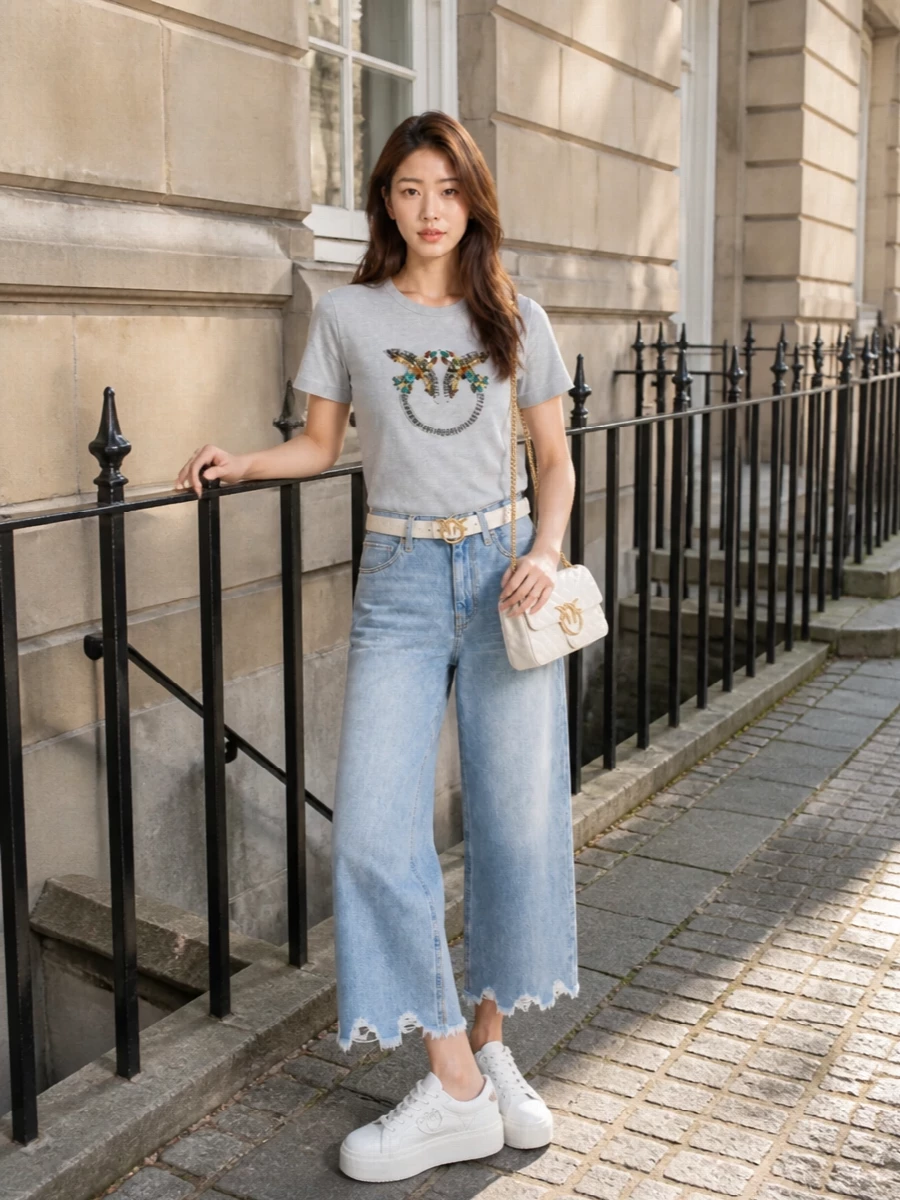 A pale embellished tee meets light-wash cropped wide-leg denim for a clean, relaxed take on city polish. Chunky white sneakers keep it easy and modern, while the ivory bag and belt echo the tee’s lightness and gold hardware for a softly coordinated finish.