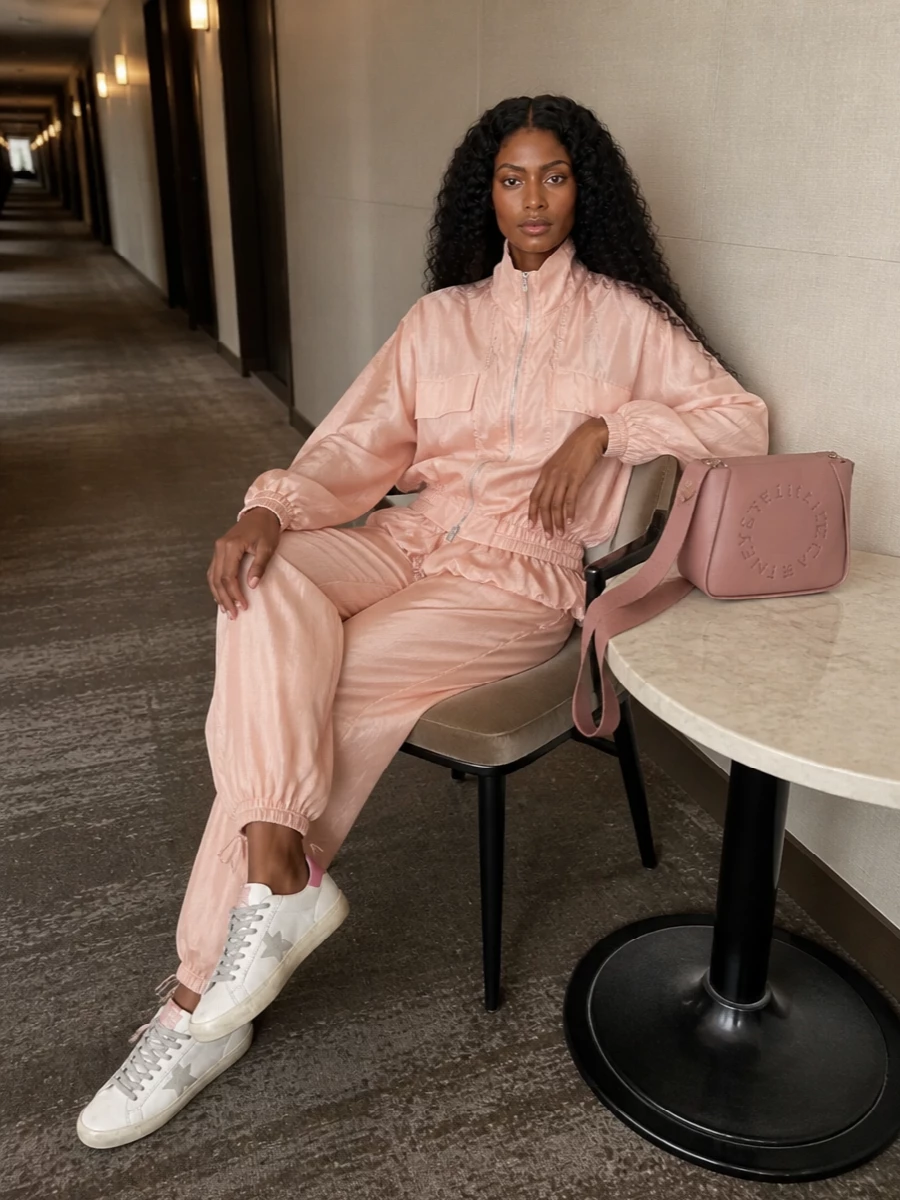 This edit leans into a soft sport mood, pairing blush technical volume on top with fluid satin track pants for a relaxed but very considered city set. The sneakers’ off white and pink details tie straight into the peachy tones, while the structured rose cross-body sharpens the ease so it reads intentional and modern rather than loungey. I chose the top and pant route over a dress because the track-inspired separates speak directly to the Golden Goose attitude and keep the vibe firmly off duty and street-ready.
