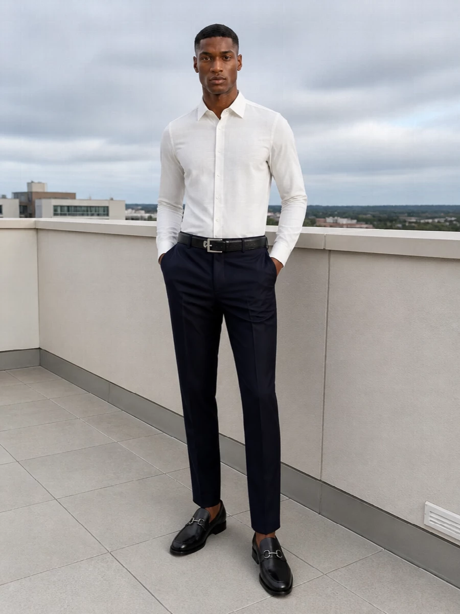 Navy tailored trousers meet a crisp ivory shirt for a clear, high-contrast take on modern business dressing. Black penny loafers, a slim belt and a structured briefcase keep the line disciplined, with silver hardware adding just enough definition. It is a precise, boardroom-ready combination that still feels relaxed enough to carry into dinner reservations after hours.