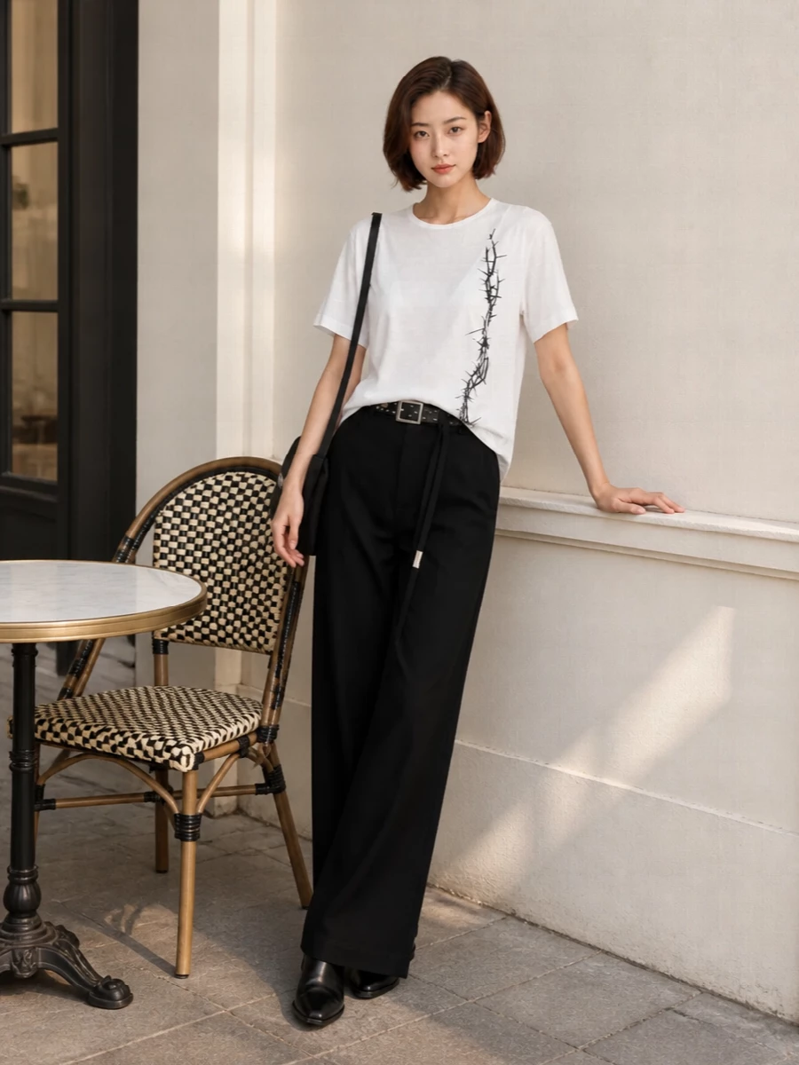Soft white and deep black stay tightly edited here, so the thorned graphic and asymmetric ties read as intentional rather than busy. The high-waisted wide-leg trouser and pointed loafer create a long, clean line, while the studded belt adds just enough hardware to keep the mood dark and poetic without tipping into costume.