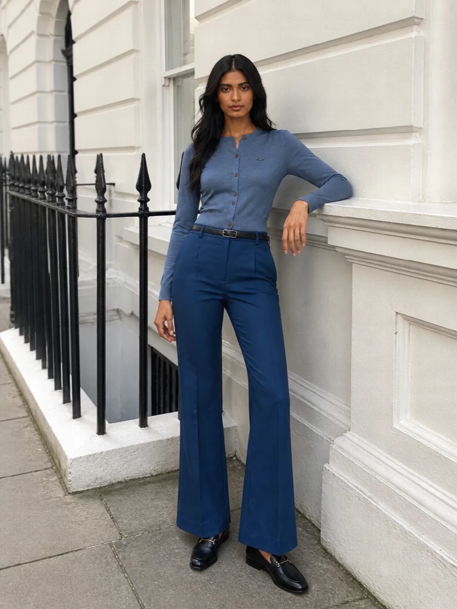 Slate blue tailoring stays soft but precise, with the cropped cardigan echoing the trouser tone to create a clean, uninterrupted line through the waist and hip. Black leather accessories ground the flared leg with quiet structure, while a slim belt and subtle hardware keep the whole outfit sharp enough for serious daytime meetings. The result is 70s-inflected suiting energy translated into a calm, modern city uniform.