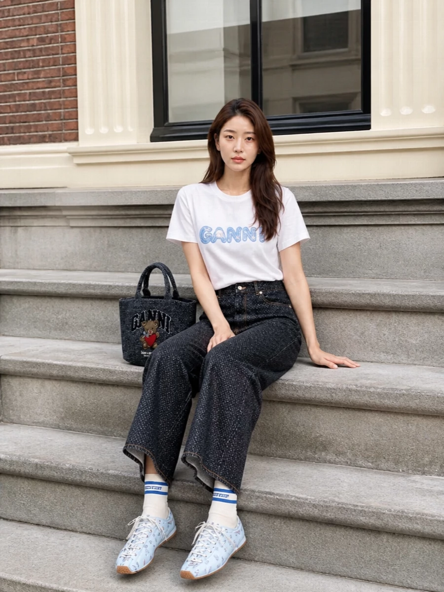 A crisp graphic tee is grounded with dark indigo wide-leg denim for a clean, relaxed line that feels street-led yet slightly preppy. Sky-blue floral lace-up flats and striped socks nod to the pastel logo and collegiate edge, while a tweedy varsity tote keeps the whole mix playful but considered for city days.