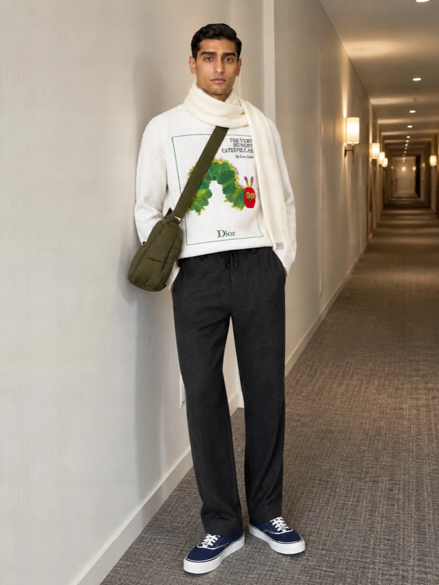 The caterpillar knit sits over precise charcoal drawstring trousers, giving the graphic top a calm, tailored base. Navy canvas sneakers keep the line relaxed and collegiate, while the olive crossbody and cream scarf echo the sweater’s colors in a quieter way for a pulled-together city finish.