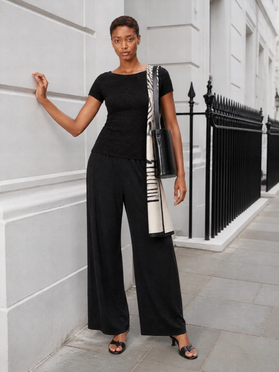 A monochrome column of subtle sparkle keeps this outfit quietly dramatic, with the knit skimming into fluid, speckled wide-legs for an elongated line. Low black slingbacks and a structured Coperni bucket hold the mood in that sweet spot between office and evening, while a graphic ivory scarf adds just enough light and structure near the face. It is refined, modern and intentionally pared back so the textures do the talking.