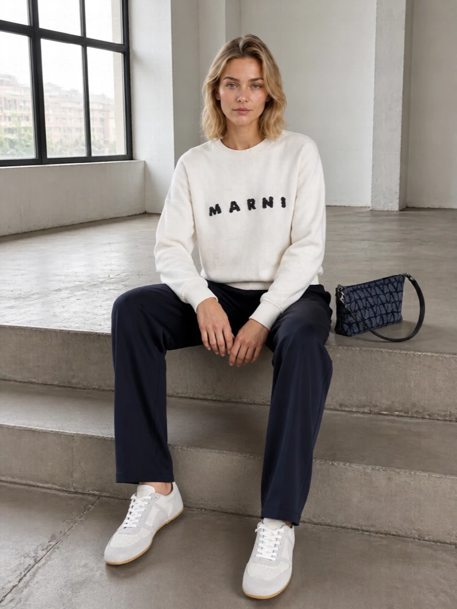 Ink navy track pants meet a slouchy off-white logo sweatshirt for a relaxed, graphic take on designer athleisure. Clean white and grey sneakers keep the line streamlined, while a structured navy shoulder bag adds just enough polish for city days without losing the off-duty attitude.
