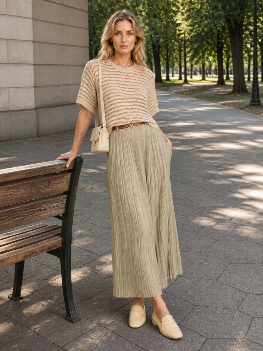 A calm sand pleated skirt meets a warm beige open‑knit, creating a soft tonal column that moves quietly from coffee run to gallery afternoon. Butter loafers and a slim tan belt add just enough structure, while a clean buttercream baguette keeps the mood modern and precise. The result is relaxed but considered, all about texture, tone, and ease in motion.