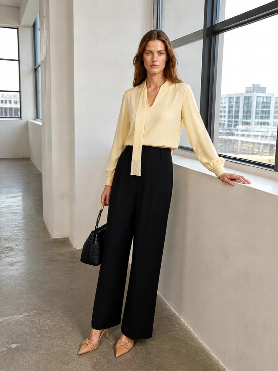 A fluid buttercream Valentino blouse is anchored by sharp black wide-leg tailoring for a long, quietly powerful column that moves effortlessly from late meeting to dinner. Nude-camel slingbacks keep the palette soft and elongating, while a black intrecciato shoulder bag adds discreet texture and gold accents for a refined, couture-leaning finish.