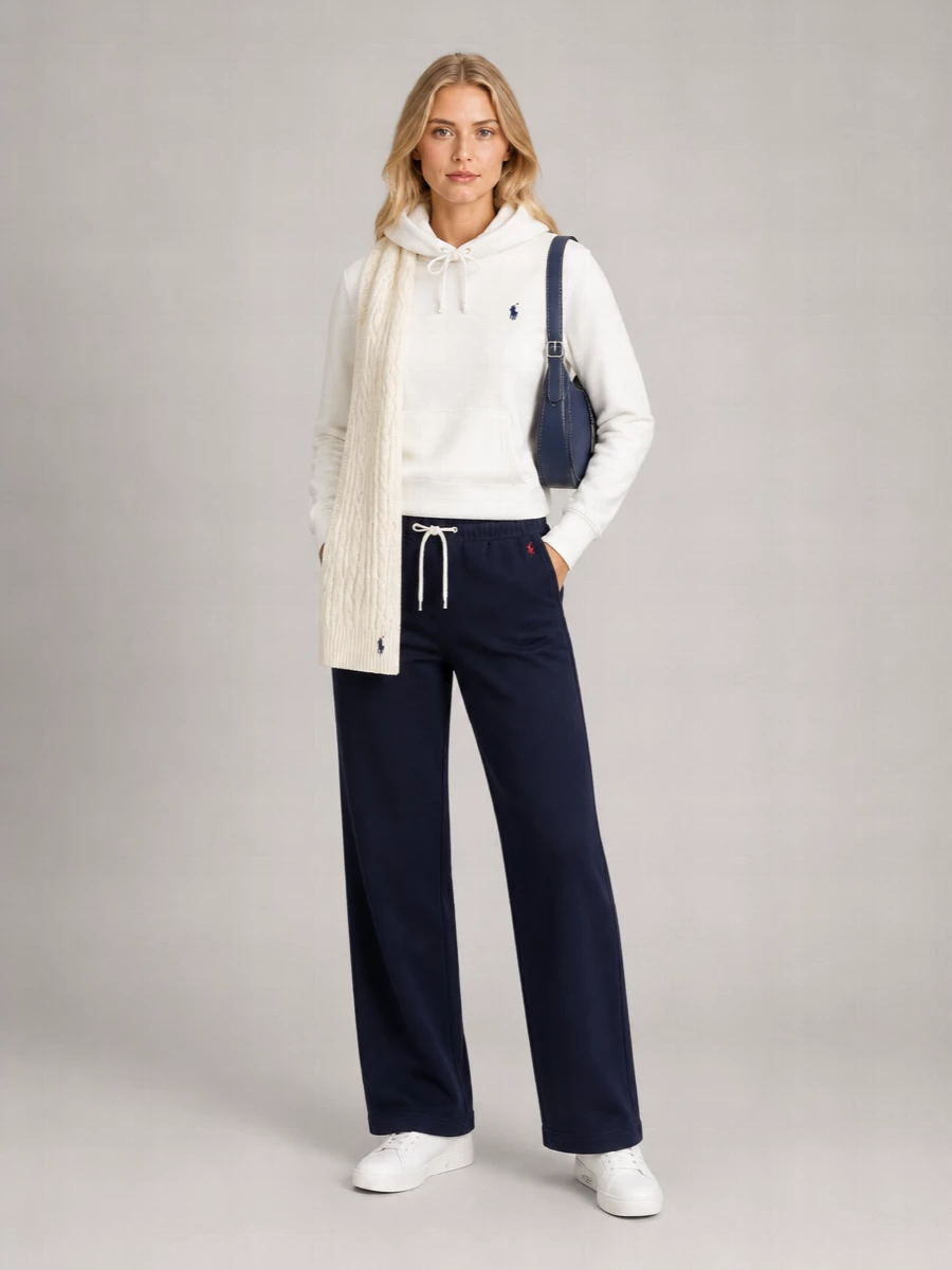 Soft white and navy stay front and center, giving this lounge set a clean campus energy instead of feeling like pure gym gear. The straight-leg pant keeps the silhouette relaxed but not sloppy, while white sneakers and a navy crossbody make it ready for coffee runs, flights or casual city days. A matching cable-knit scarf finishes the story with a subtle repeat of the hoodie’s iconic pony detail.