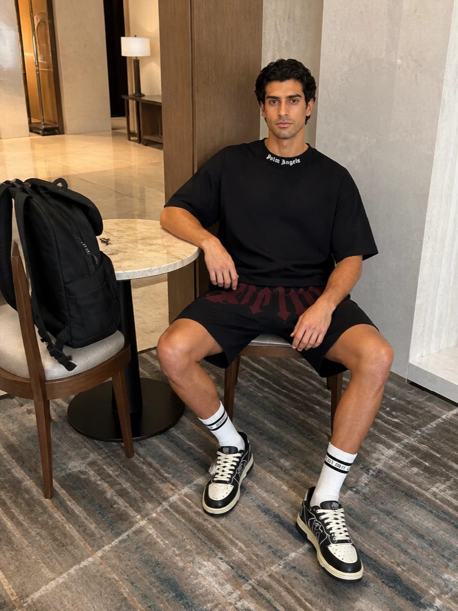 Head to toe in deep monochrome, this outfit lets the burgundy logo across the shorts do the talking while the black boxy tee and skate-inspired sneakers keep the lines clean and relaxed. The Palm Angels backpack and striped socks bring a low-key stadium feel, so you move from street to bleachers without changing a thing.