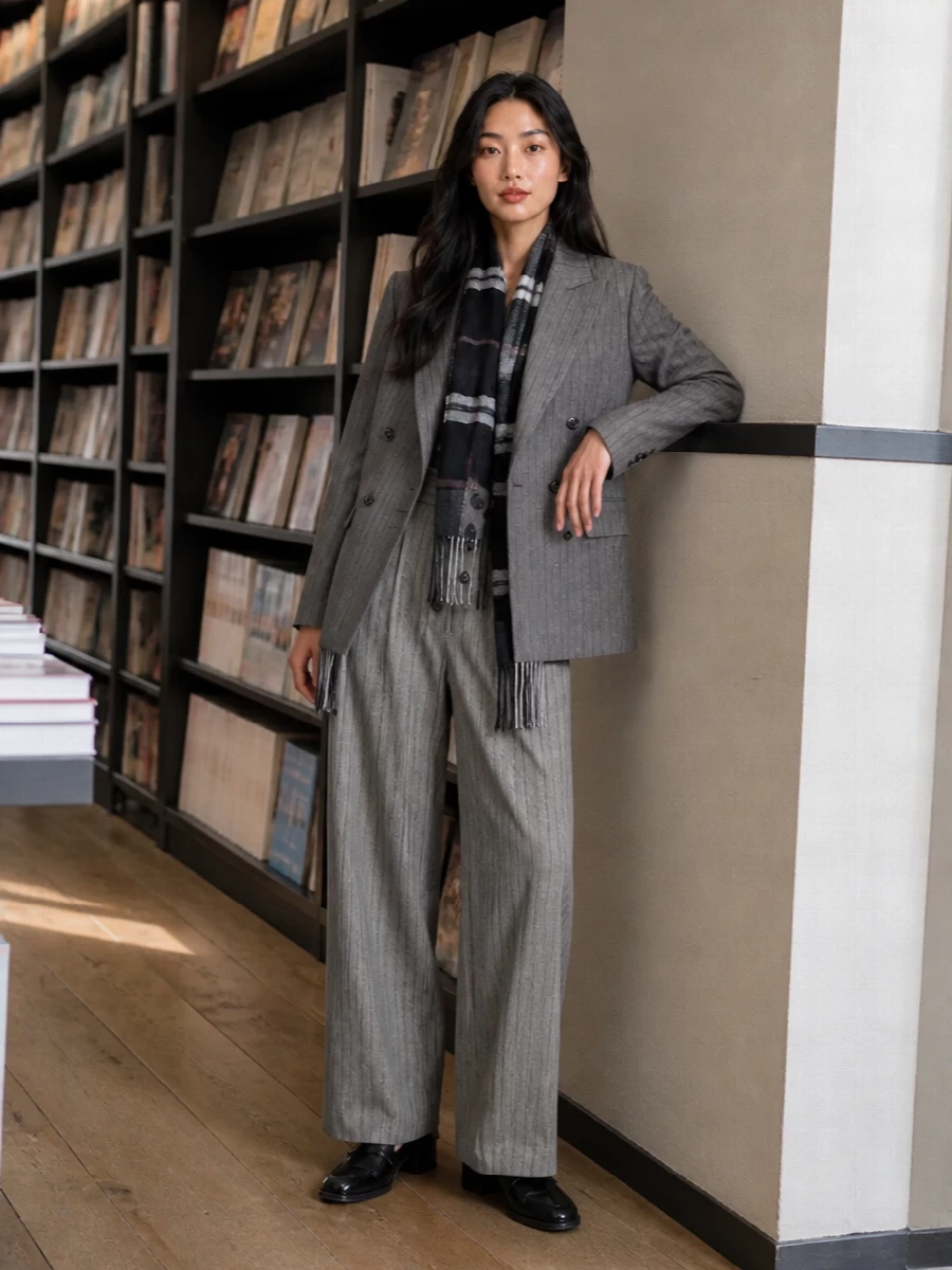 Grey pinstripes on top of soft herringbone trousers create a nuanced, tailored column that feels confident but never severe. Glossy black loafers and a croc-embossed top-handle keep the suiting firmly in modern city territory, while the monochrome check scarf adds just enough heritage texture. It is a quietly assured outfit for days that run from strategy meeting to late dinner reservation.