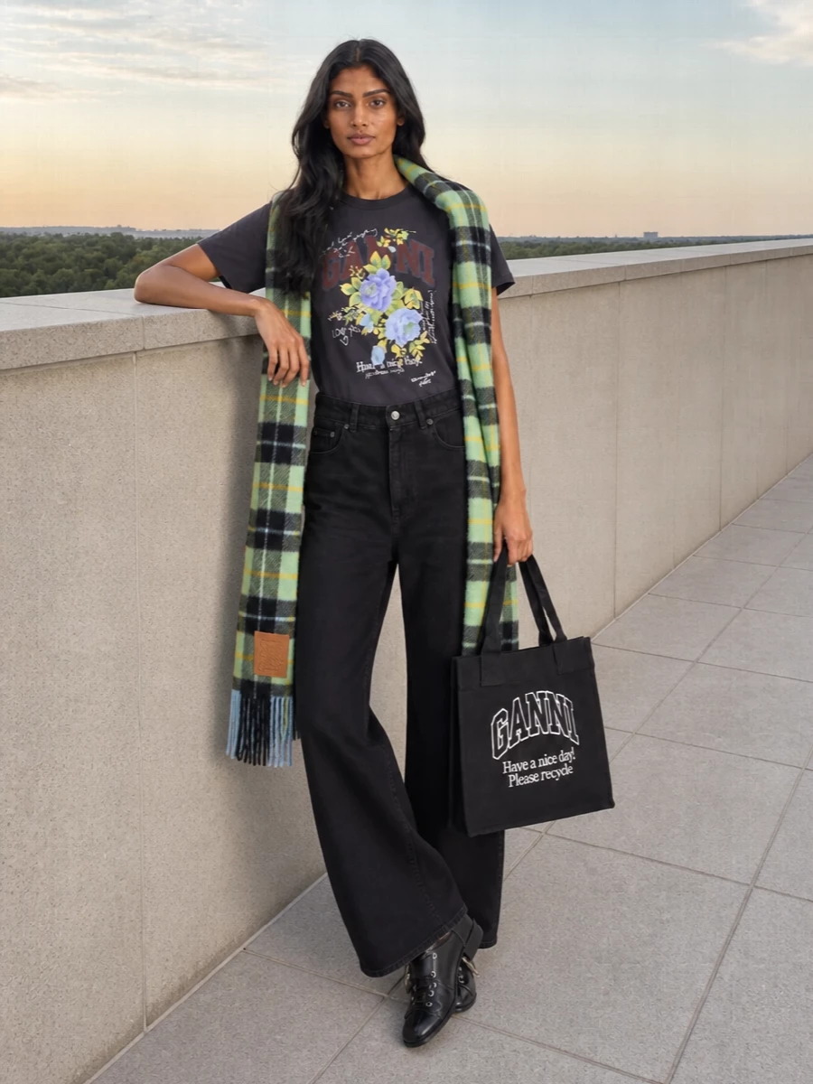 Charcoal graphics sit against relaxed wide-leg black denim for a soft grunge take on Ganni streetwear. Lace-up boots and a collegiate tote keep it practical and city ready, while the pastel check scarf brings a hit of color that still talks to the tee’s florals.