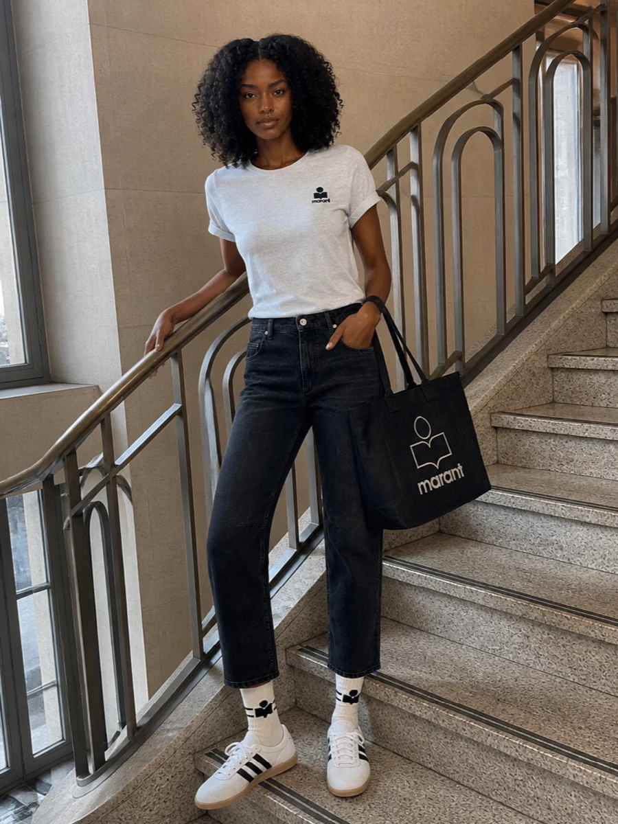 A soft heather tee and washed charcoal denim create a monochrome base that feels relaxed yet considered. Retro low-top sneakers and a structured logo tote keep the mood casual but sharp, ideal for all-day city wear with a subtle Parisian edge.