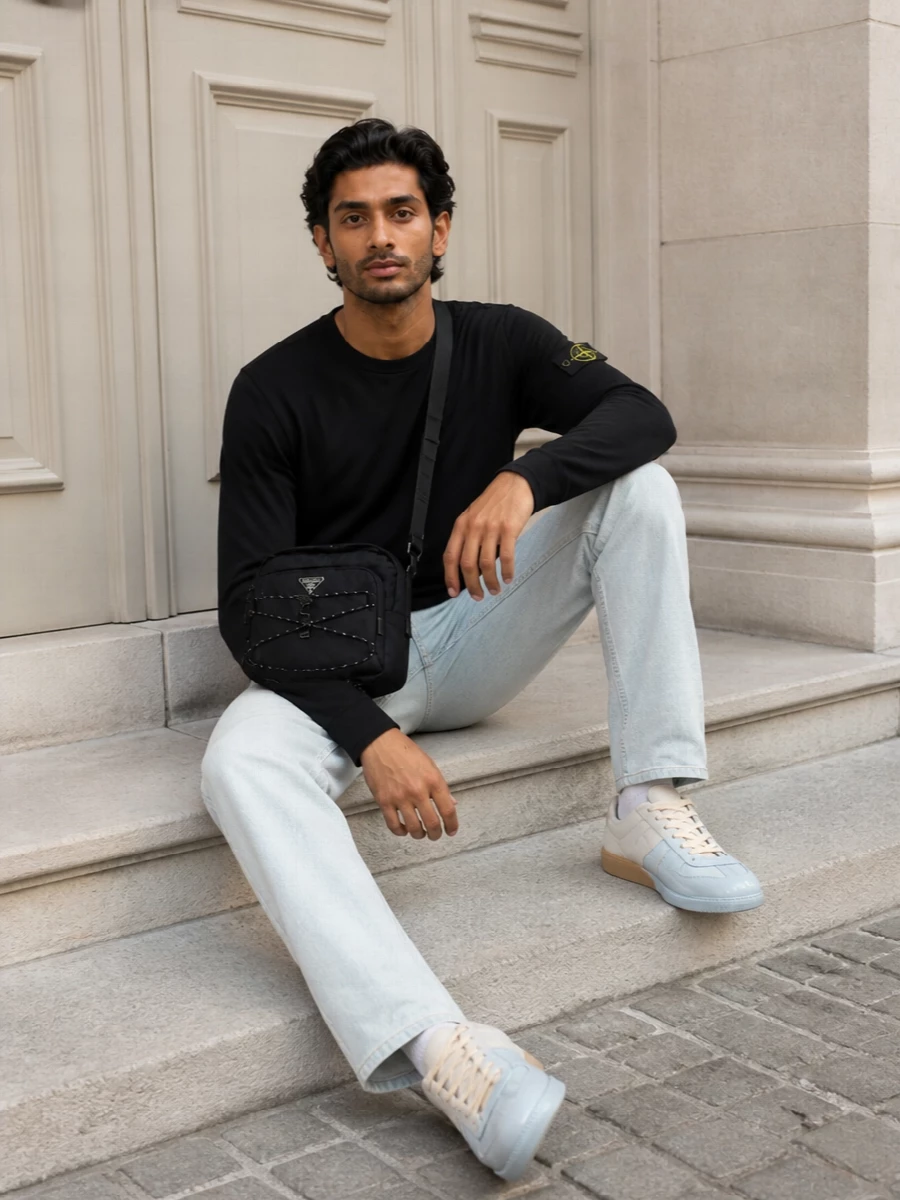 A black Stone Island long-sleeve sits against icy straight-leg denim for a clean, badge-led street uniform in a tight black and pale blue palette. Margiela’s dip-dyed sneakers mirror the denim tone without shouting, while the structured Prada crossbody keeps everything city-ready and streamlined. The result is relaxed, technical and intentional, with each piece quietly reinforcing the same graphic, modern mood.
