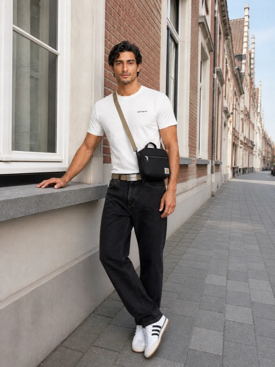 An off-white Carhartt tee sits against washed-black denim for a tight, monochrome street uniform that feels easy but considered. The retro Adidas trainers keep the line slim and agile, while the small black crossbody and sand belt add just enough utility detail without cluttering the silhouette.
