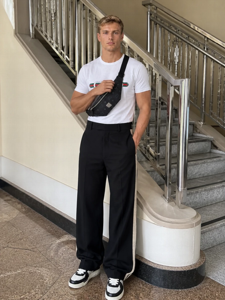 A Gucci logo tee sets a crisp white base against black wide-leg Palm Angels trousers for a relaxed, sport-lean silhouette. Chunky Amiri sneakers echo the monochrome story, while the MCM belt bag keeps it city-functional and firmly in the luxury streetwear lane. The proportions stay easy and long, with the tee sitting boxy over a fluid, pooling leg and a strong sneaker platform at the hem.