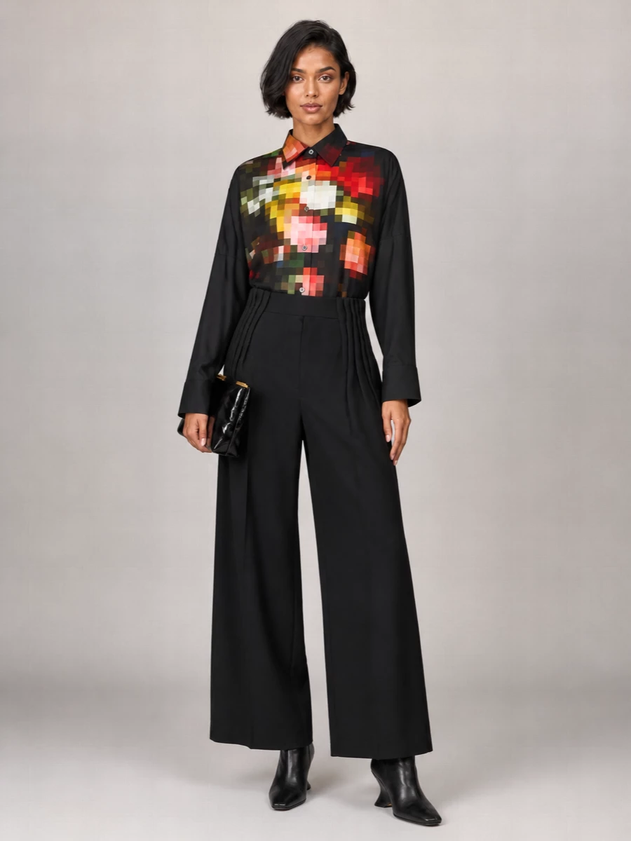 The pixelated Dries shirt sits over a deep black high-rise wide leg, so the color and print read as a single, elongated statement rather than being broken up. Sculpted black ankle boots keep the line sharp and directional, while a glossy oversized clutch and a painterly silk scarf add just enough texture and artistry without crowding the shirt’s graphic front. It is precise, modern city tailoring with a distinctly art-led mood.