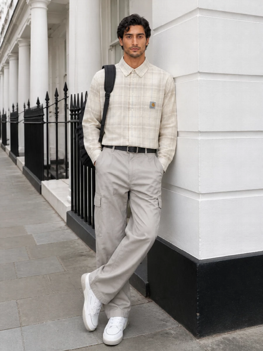 Stone-grey cargos meet a washed cream plaid shirt for a light, utilitarian take on casual city dressing. Off-white and grey Represent sneakers keep everything grounded and modern, while a black tactical-leaning backpack and clean belt add just enough structure. The result is relaxed, practical and coherent in tone, ideal for long days moving between skate, commute and hangouts.