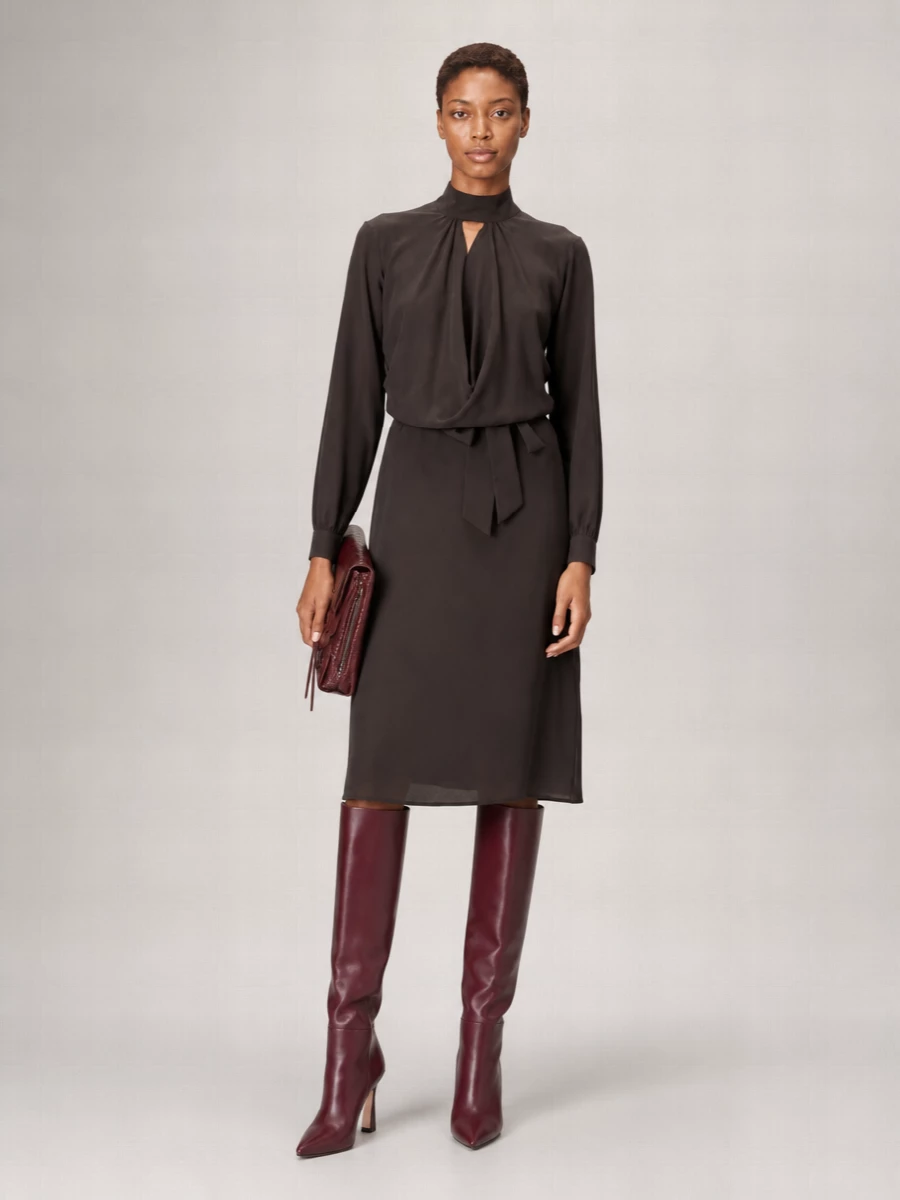 This pairing leans into a single dark, sculpted column: the espresso midi dress and burgundy boots work tone-on-tone for a sophisticated, boardroom-to-dinner presence. The clean knit and fluid skirt line let the boots’ flared heel and pointed toe read as the only deliberate edge, keeping the mood quiet rather than showy. The burgundy clutch finishes it with a controlled hit of gloss that still feels restrained and modern.