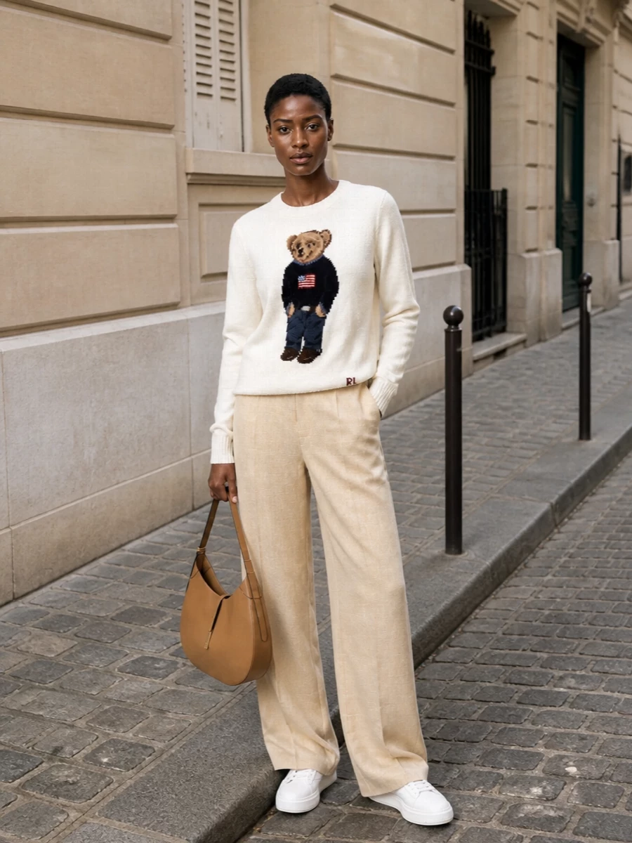 Polo Bear goes Riviera preppy with sun-washed wide-leg tailoring and a clean, neutral sneaker. The high-rise beige trouser lengthens the line, while the tan hobo picks up the knit’s warm camel tones for a relaxed yet considered finish.