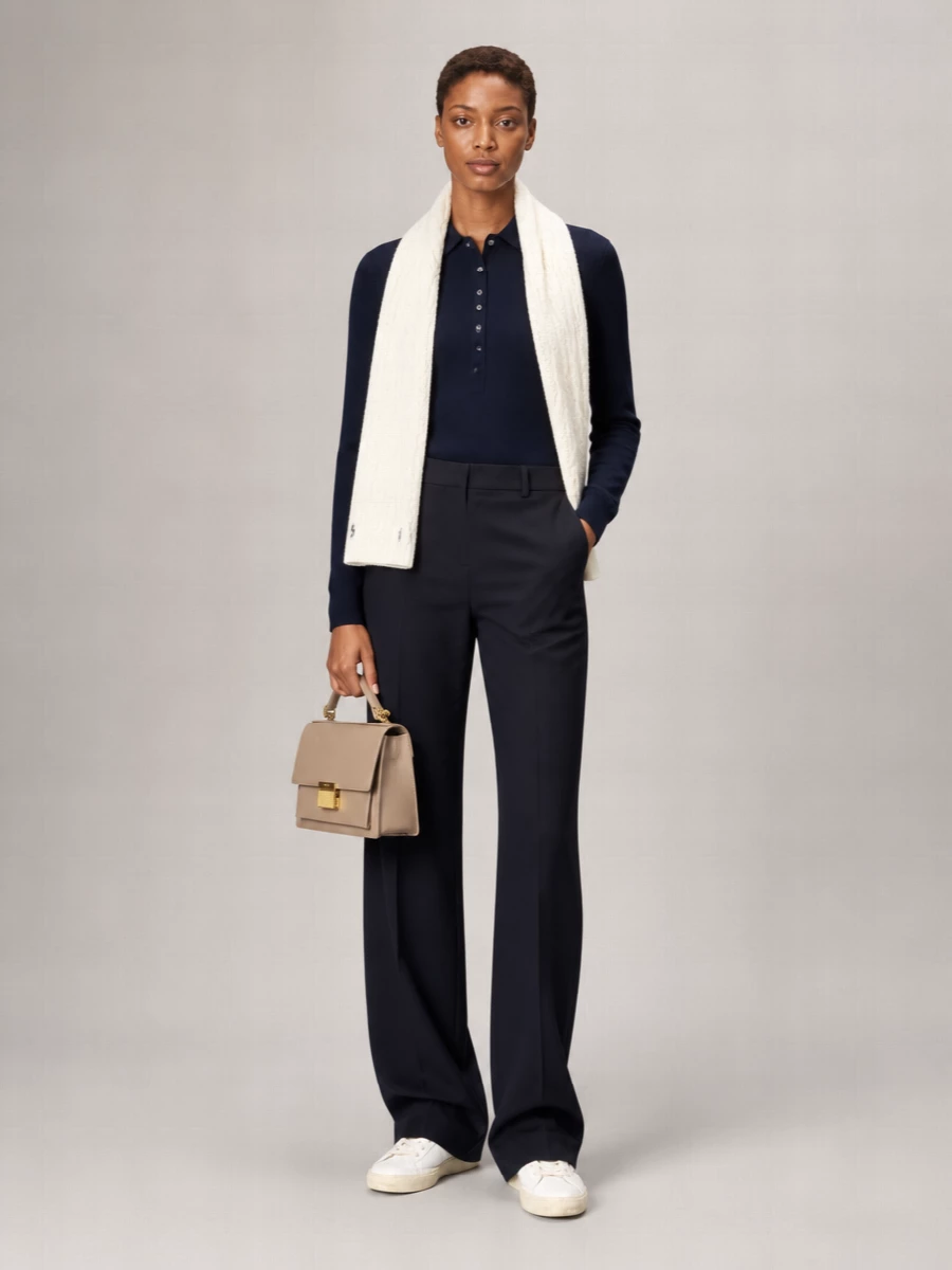 Deep navy on navy builds a clean, elongating line, with the tailored trouser sharpening the polo knit into something office ready yet relaxed enough for off-duty. Off-white sneakers and a taupe top-handle keep the palette soft and modern, while the winter white scarf brings a collegiate note that still feels grown up. The result is quietly polished, minimal and easy to wear on repeat.