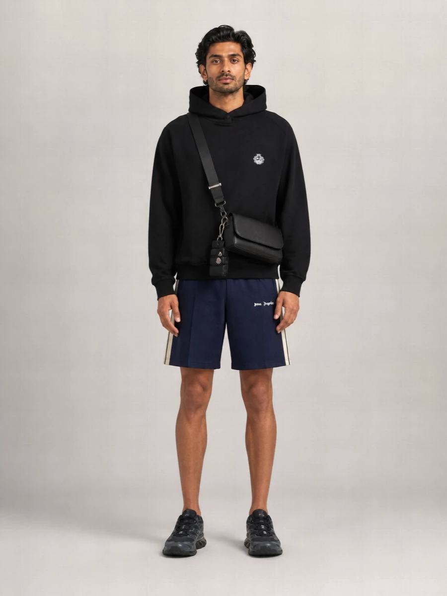 A black hoodie, navy track shorts and technical runners frame the Moncler mini gilet charm as a subtle flex, not a costume. The palette stays tight in black, navy and cream so the logos and hardware read as considered hits, not clutter. The McQueen belt bag finishes it with hands-free utility that feels right for city laps, airport transits or low-key weekends around town.