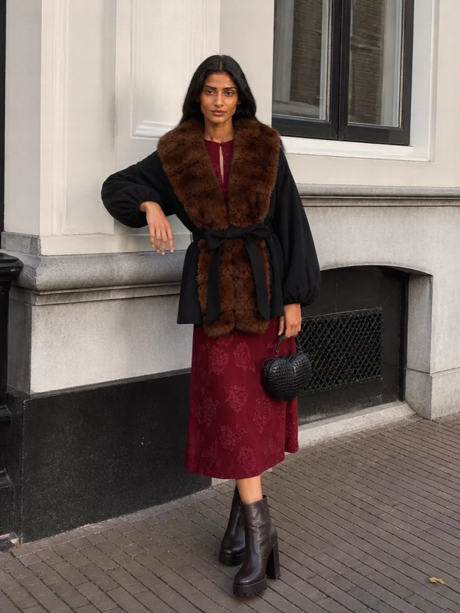 I chose the dress route, pairing the romantic burgundy jacquard midi with the faux‑fur collar coat for a cohesive, winter‑ready cocktail story that lets the coat frame a clean hourglass silhouette. Dark chocolate platform boots keep it grounded yet glamorous, while the black heart bag ties back to the coat’s base and nods to Rotate’s playful edge. The result is romantic, warm and city‑evening appropriate without feeling over‑the‑top formal.