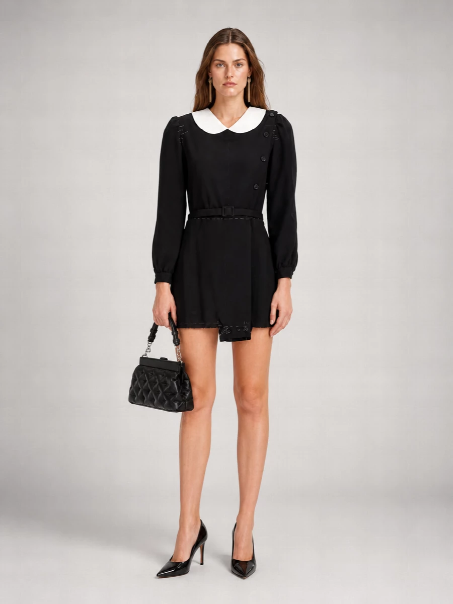 A prim, subversive Margiela mini is sharpened with glossy black stilettos and a compact quilted shoulder bag, keeping everything graphic and controlled around the collar’s stark contrast. Long gold tassel earrings and a fine chain at the waist introduce just enough movement and warmth, so the whole ensemble reads polished, slightly off-kilter, and ready for gallery nights or dark-panelled bars. It is strict from a distance, but the closer you get, the more the textures and details start a conversation.