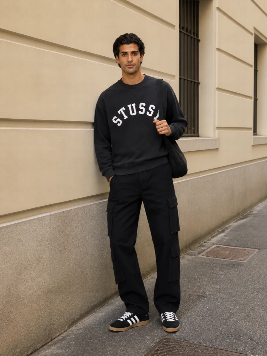 Stüssy’s washed black crew sits over sharp black cargo trousers for a clean, graphic street uniform. Adidas terrace sneakers in black, white and gum keep the nod to skate and terrace culture, while the padded Balenciaga shoulder bag adds a stealth-luxe edge without breaking the casual mood.