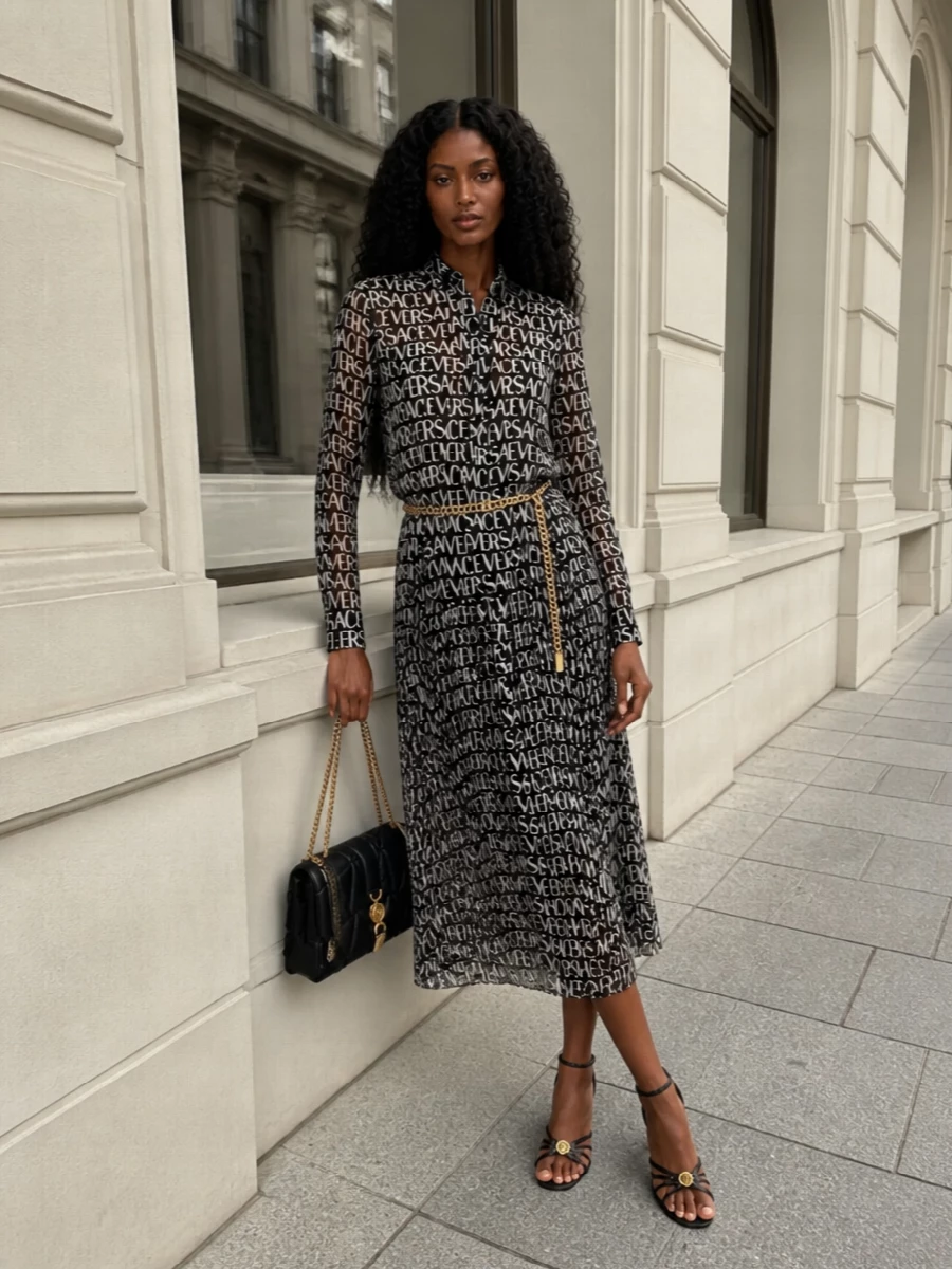 A graphic Versace logo dress is grounded in a strict black and gold story, letting the typography stay center stage. Strappy mid-heel sandals and a quilted chain bag bring just enough hardware to feel decadent, while a slim chain belt adds subtle definition without interrupting the fluid line. The result reads confident and modern, ideal for a gallery afternoon that slides straight into cocktails.