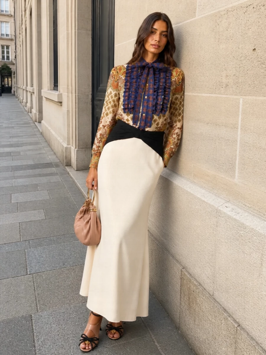 This look frames the paisley bow blouse with a sculpted cream-and-black maxi skirt, letting the print’s cobalt and burnt orange sing against a clean, elongated column. Nude-and-black stilettos and a soft blush clutch keep the palette warm and polished, delivering a romantic, dressy SS ensemble that feels opulent yet controlled above the table. A whisper-light logo scarf adds a final, optional layer of Valentino drama while maintaining the outfit’s poised, tailored balance.