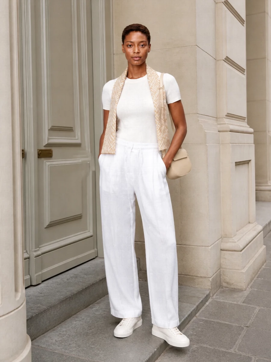 A slim ribbed tee and fluid white wide-leg trousers create a long, tonal line that feels calm and understated. Clean white sneakers keep it relaxed but polished, while the buttercream shoulder bag and soft neutral scarf add just enough structure and texture. It is an easy warm-weather uniform for city days when you want subtle quiet luxury rather than sharp tailoring.