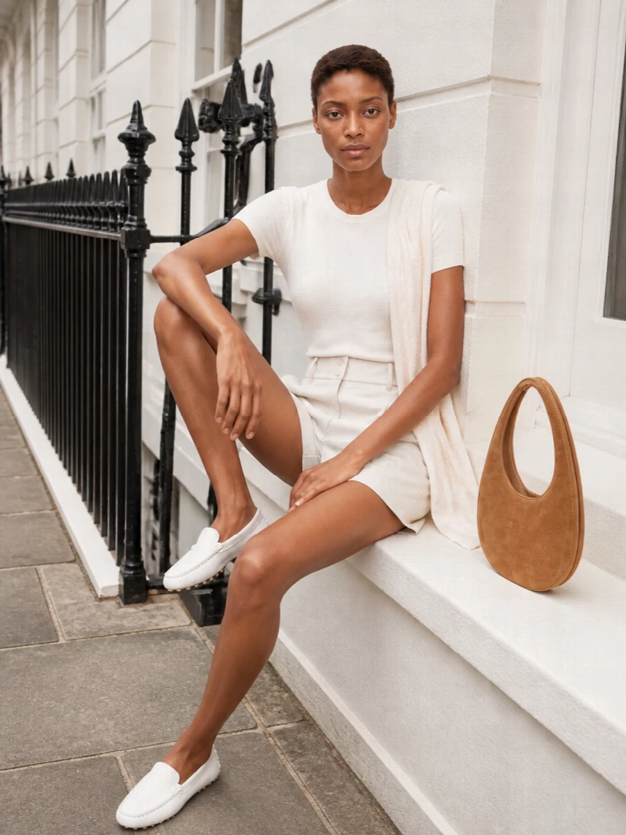 An ivory knit tee pairs with tailored high-waist shorts for a clean, sun-ready take on city dressing. White driving loafers keep the line streamlined, while a camel suede shoulder bag adds just enough warmth and texture. A whisper-light neutral scarf finishes everything with a soft, intentional touch.