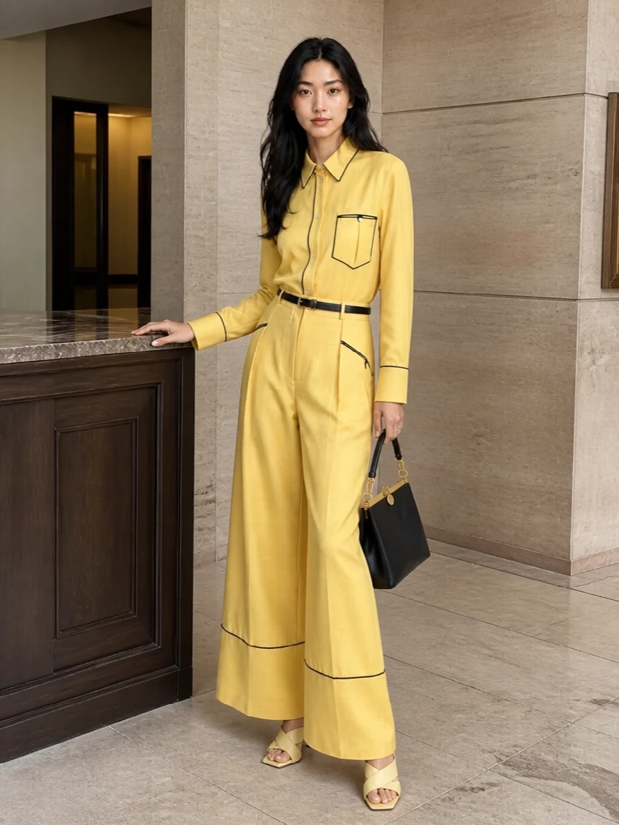 Head-to-toe sunshine yellow tailoring, traced with black piping, reads confident and graphic yet still quietly luxurious. Butter-toned heels soften the impact while a structured black top-handle and fine black belt give the color a disciplined, architectural frame. The result is summer tailoring that feels as sharp in a boardroom as it does at a rooftop dinner.