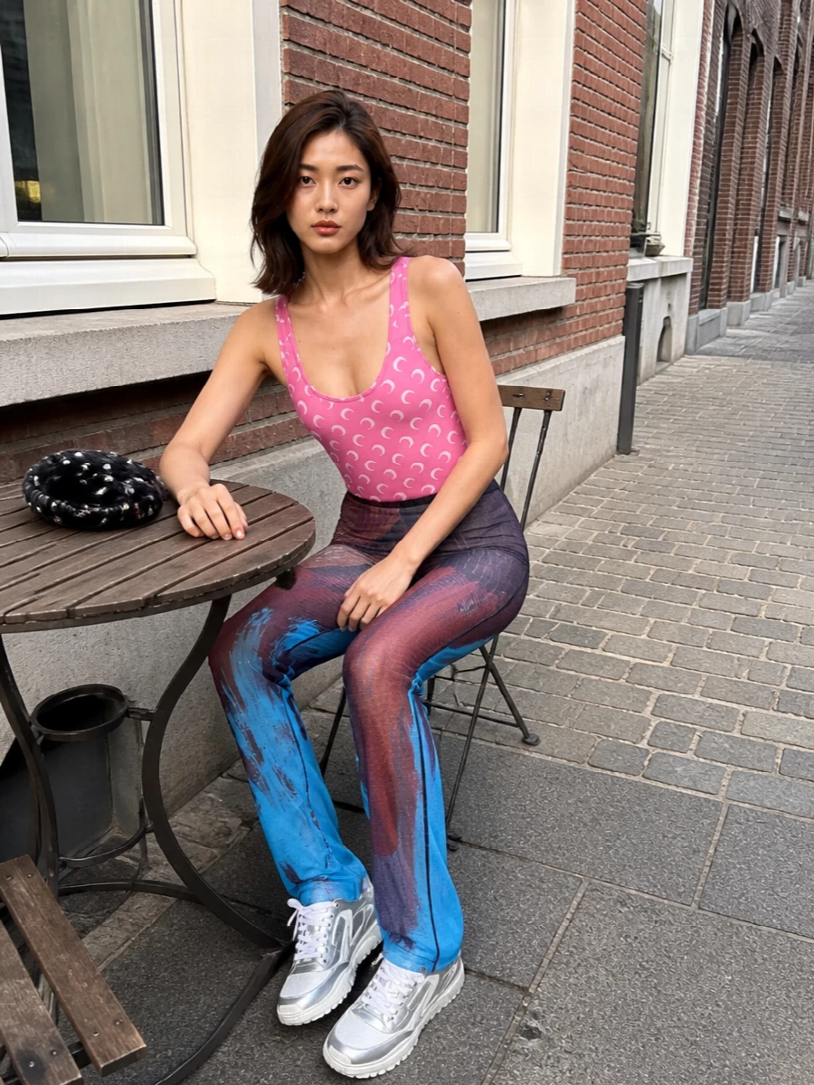 Marine Serre’s pink moon-print bodysuit meets Gaultier’s sheer mesh pants for a late-night, body-conscious take on sport. Silver-detailed Dior sneakers keep it fast and futuristic, while the studded Khaite crescent bag adds just enough dark gloss to make it feel party-ready rather than gym-bound.