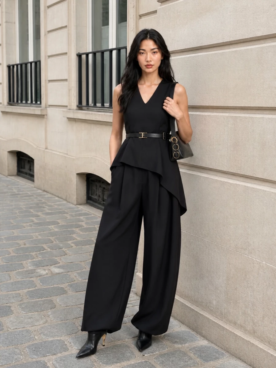 A pure black, sculptural evening ensemble that plays with volume on the bottom and controlled structure on top. The asymmetric peplum echoes the trouser’s wrap front, while pointed boots and a slim shoulder bag keep the proportions long and sharp. Subtle gold hardware and a fine belt detail add just enough light without breaking the quiet, tailored mood.