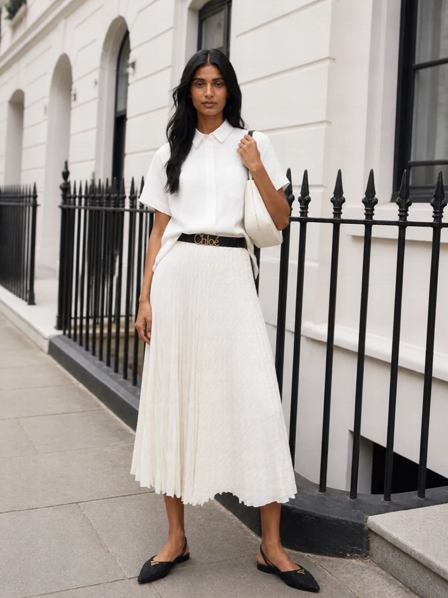 A crisp white architectural shirt meets the pleated ivory Sacai skirt for a sharp, quietly luxurious take on monochrome tailoring. Flat pointed black Prada slingbacks and an off-white crescent bag keep the palette light yet precise, with the optional black belt adding definition if you want a more structured waist. The result is polished enough for client-facing days yet fluid and modern for gallery evenings or dinner in the city.