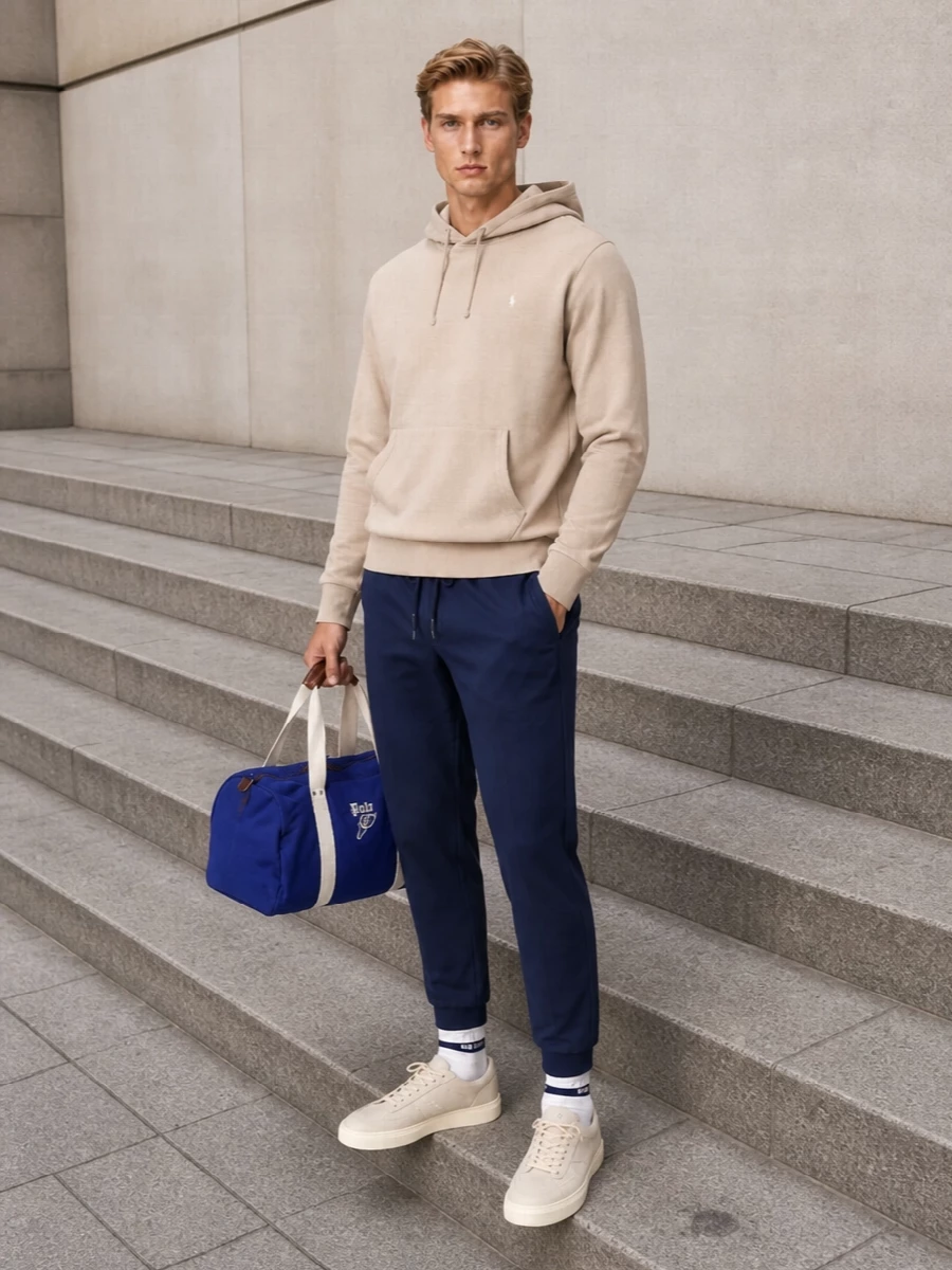 A neutral Polo hoodie sits cleanly over straight-cut navy joggers for a calm, collegiate take on athleisure. Soft-ivory Hogan sneakers and striped socks keep the palette light and considered, while the royal-blue duffle injects just enough sport energy for campus runs, coffee stops or relaxed travel days.