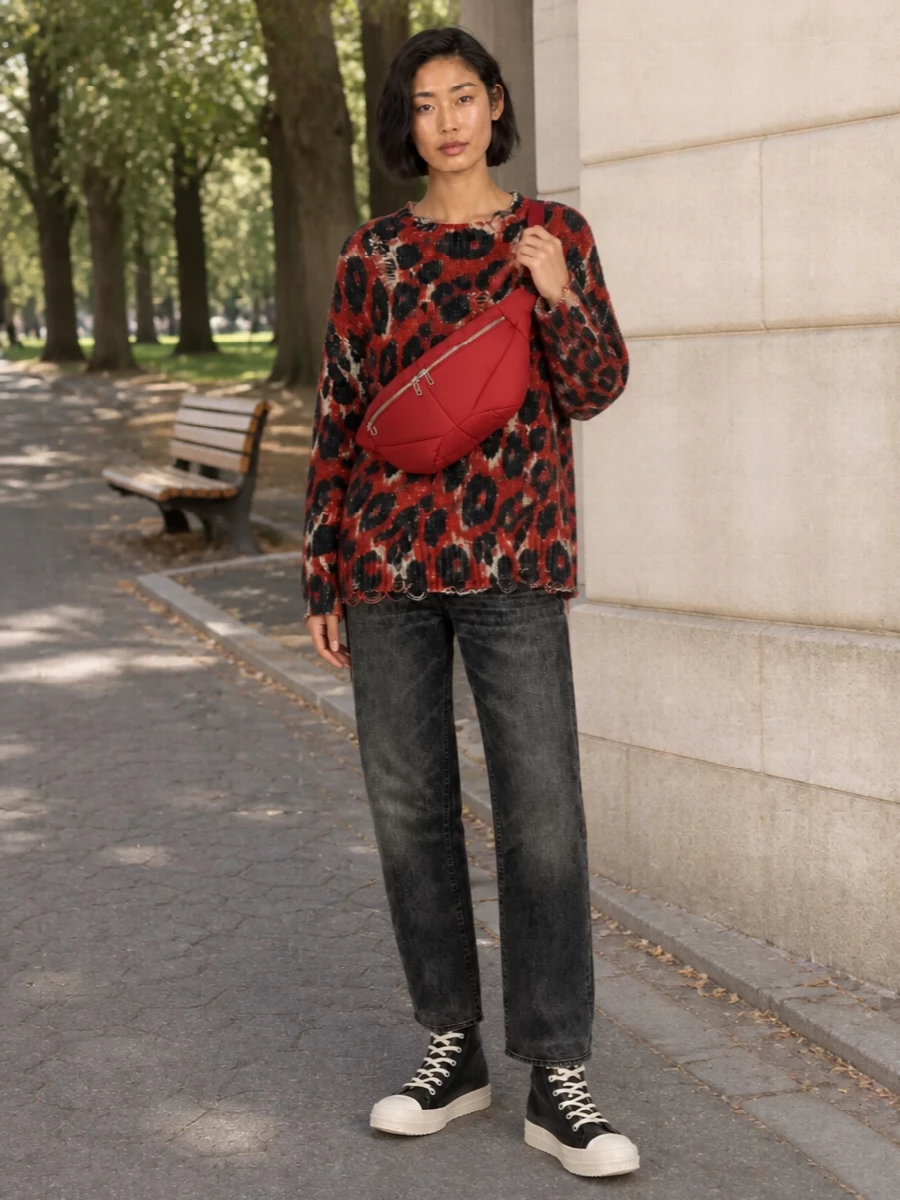 An oversized, shredded animal knit in brick red is grounded with washed-black straight R13 denim for a grunge-heavy, downtown feel. Chunky black-and-ivory Rick Owens high-tops and a brick padded belt bag keep the palette tight and the attitude sharp. The result is a slouchy yet precise streetwear uniform that feels pulled together without losing its raw edge.