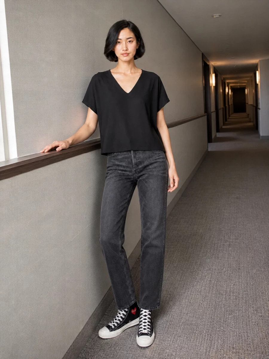 Straight charcoal denim grounded with a fluid black V-neck tee creates a clean, low-key base that still feels intentional. High-top canvas sneakers keep it street but unfussy, while the structured black bucket bag adds a precise, polished edge. The result is a quietly strong monochrome outfit that works from coffee runs to late nights without needing a change.