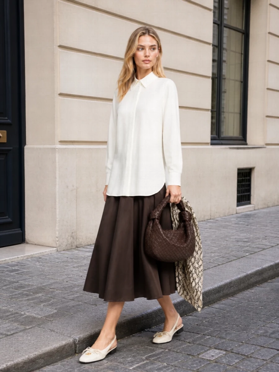 A deep chocolate flared midi anchors the look, paired with a fluid ivory longline shirt for an effortless, minimalist take on quiet luxury. Ivory mesh slingback ballerinas keep the silhouette light and polished, while a slouched chocolate intrecciato hobo and a sheer ivory logo scarf add tactile depth and discreet house signatures. The result is a refined SS ensemble that moves seamlessly from daytime appointments to understated evening plans.
