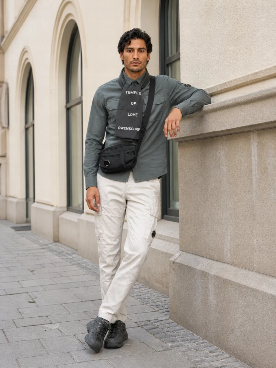 Slate grey on top and light stone below keep the palette cool and minimal, while the articulated cargos echo the shirt’s utility detailing. Charcoal trail runners and a compact lens crossbody ground everything in a tech-forward streetwear mood, with the gauzy scarf adding a quiet graphic twist if you want an extra layer of attitude.